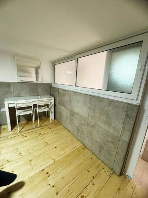 Moderna cucina con tavolo da pranzo, due sedie, rivestimento in piastrelle grigie e pavimento in legno a Neapolis