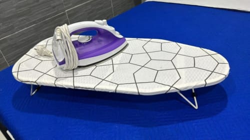 Purple and white steam iron with coiled cord on ironing board at Neapolis Tecnotourist apartment in Italy