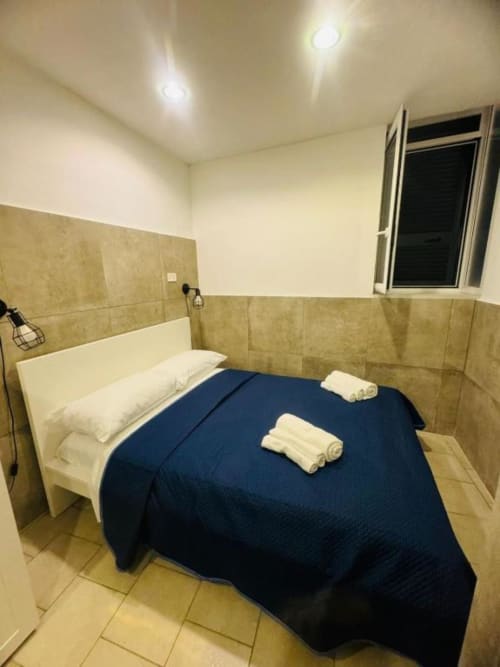 Bedroom at Neapolis Tecnotourist BnB with bed, white pillows, rolled towels, and beige tiled walls