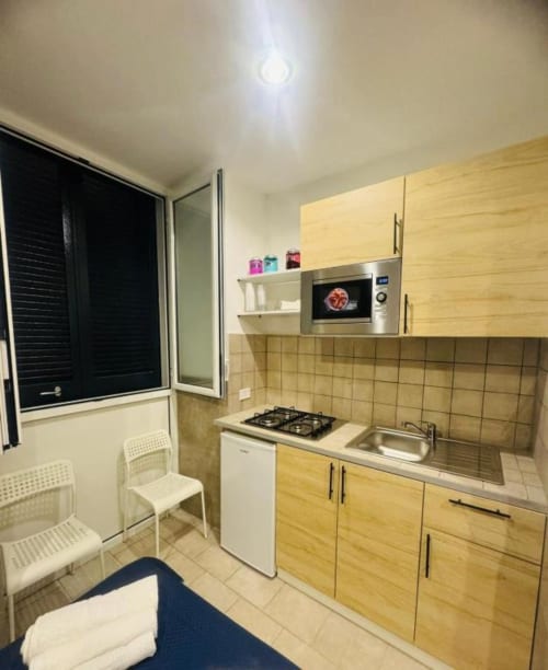 Modern kitchen in Neapolis Tecnotourist apartment with wooden cabinets, gas stove, microwave, sink, and dining area with blue