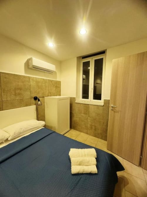 Camera moderna a Neapolis Tecnotourist con letto blu, cuscini color crema, arredamento in tonalità legno, aria condizionata e giardino