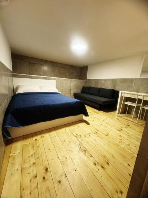 Camera spaziosa con pavimenti in legno, letto blu, divano nero e servizi moderni presso l'appartamento Neapolis Tecnotourist in Italia