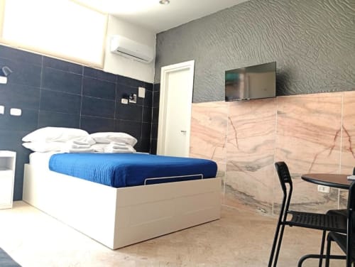 Modern bedroom at Neapolis Tecnotourist with blue bedding, flat-screen TV, desk area, and marble-style wardrobe