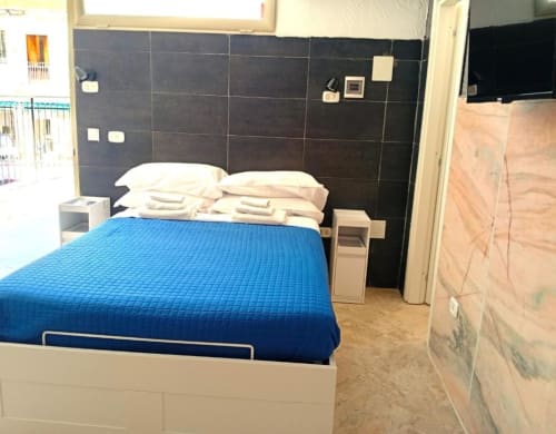 Neapolis Tecnotourist quadruple room with blue bedding, black tile headboard, wooden floor, and modern amenities in Naples,