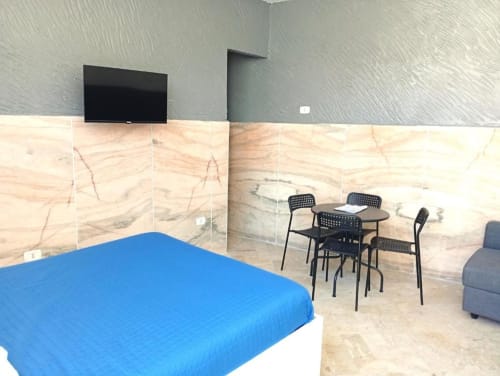 Modern hotel room at Neapolis with blue bed, black dining table, marble walls, flat-screen TV, and contemporary decor