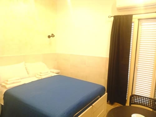 Neapolis Tecnotourist double room with blue bed, cream walls, dark curtains, and terrace access door in Italy
