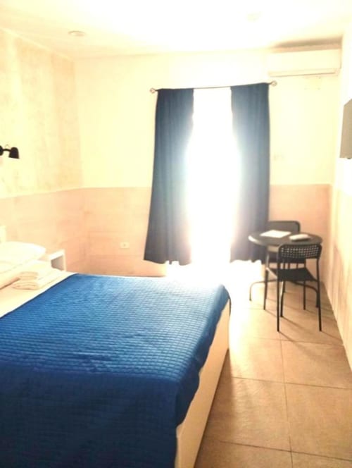 Neapolis Tecnotourist double room with blue bed, dark curtains, tile flooring, and city view window