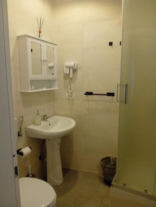 Modern bathroom at Neapolis Tecnotourist with pedestal sink, toilet, tile walls, and shower area