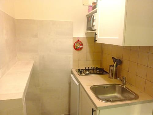 Small kitchenette with stovetop, sink, and yellow tiled walls in Neapolis Tecnotourist double room with terrace in Italy