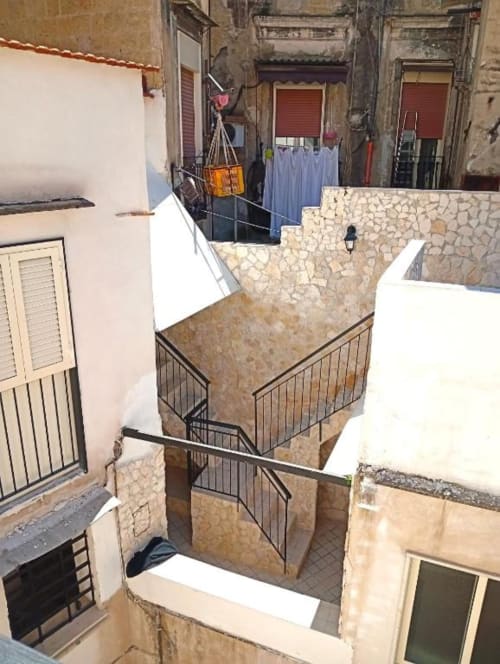 Neapolis Tecnotourist courtyard view with stone stairs, metal railings, and surrounding residential buildings in Italy