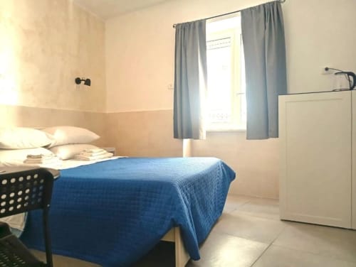 Bright double room with blue bedspread and city view at Neapolis Tecnotourist B&B in Italy, featuring modern amenities and