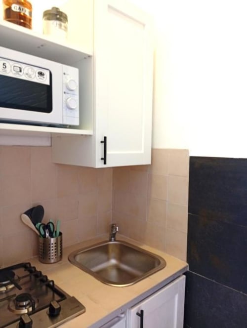 Compact kitchenette with white microwave, gas stovetop, stainless steel sink, and beige tile backsplash in Double Room at