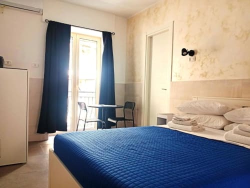 Modern double bedroom with blue bedcover, balcony access, and city views at Neapolis Tecnotourist, Italian B&B