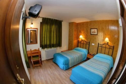 Habitación doble del Hotel Llibrada en Benasque con edredones azules, suelos de madera, iluminación cálida y vistas a las montañas