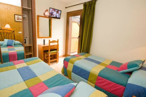 Luminosa habitación doble en Hotel Llibrada de Benasque con ropa de cama patchwork colorida, muebles de madera y vistas a la montaña