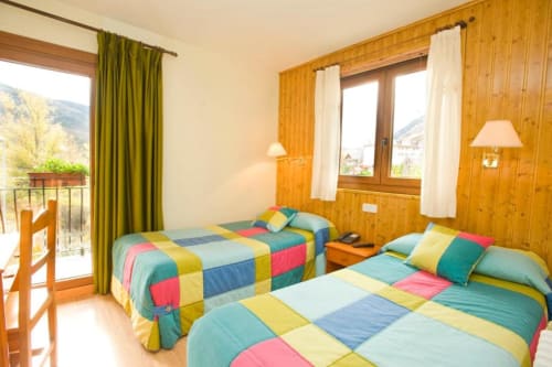 Luminosa habitación doble en Hotel Llibrada de Benasque con camas acolchadas coloridas, paredes de madera, vistas a las montañas desde el balcón y