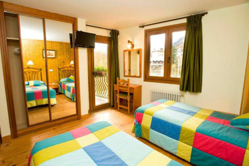 Habitación doble luminosa en Hotel Llibrada de Benasque con colchas coloridas, armarios con espejo y vistas a las montañas desde el balcón