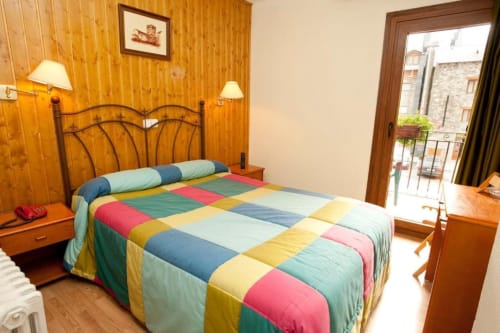 Habitación doble con edredón colorido en Hotel Llibrada de Benasque, con paneles de madera y balcón con vistas a la montaña