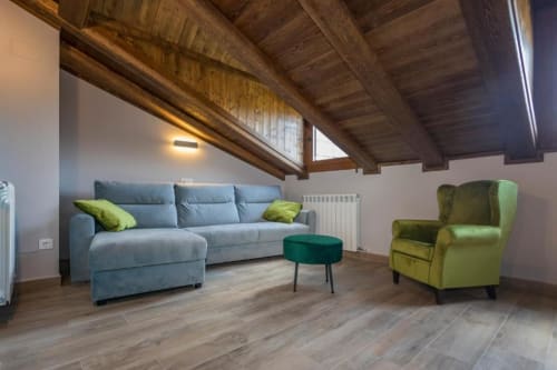 Sala de estar estilo loft moderno en apartamento de Benasque con vigas de madera vista, sofá gris, butaca verde chartreuse y montaña