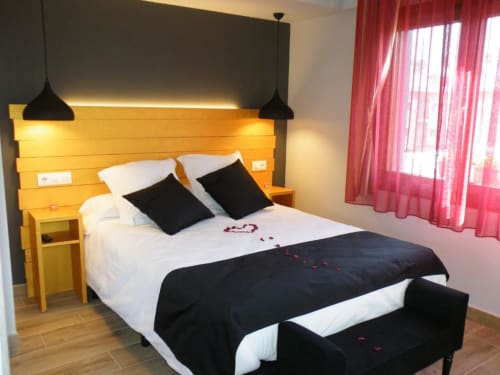 Dormitorio moderno del Hotel Llibrada en Benasque con cabecero amarillo, lámparas colgantes negras y cortinas rojas con vistas
