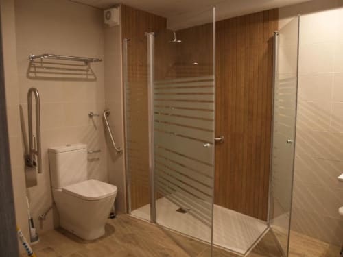 Baño moderno con ducha walk-in, inodoro y piso de baldosas imitación madera en los Apartamentos El Puente, hotel Benasque