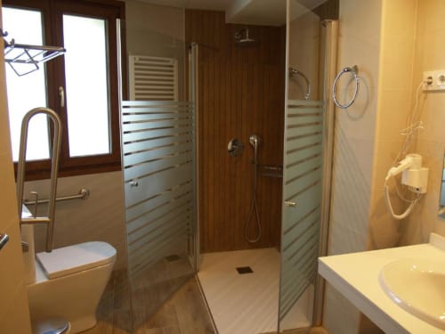 Baño moderno del apartamento Hotel Llibrada en Benasque, con azulejos amarillos, ducha a ras de suelo, inodoro y lavabo.
