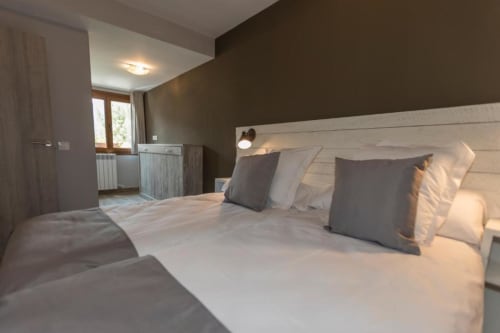 Dormitorio moderno en El Puente Apartments del Hotel Llibrada, Benasque, con vistas a montaña, cama blanca y almohadas grises