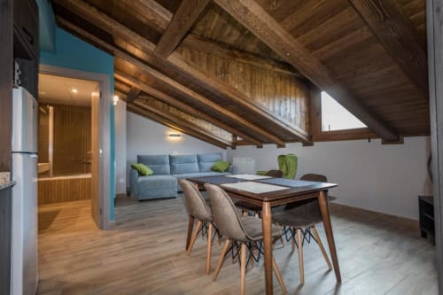 Moderno loft en Benasque con vigas de madera, mesa de comedor, sofá azul y vistas a la montaña
