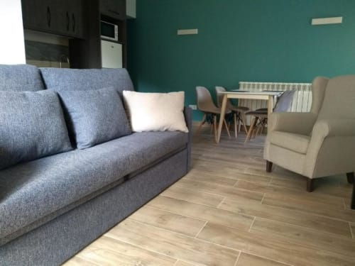Sala de estar moderna del Hotel Llibrada con sofá azul, sillón beige, suelos de madera y pared de acento en tonos azul verdoso