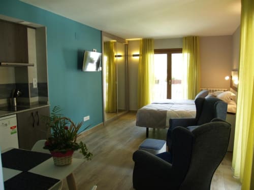 Estudio en el Hotel Llibrada de Benasque con paredes turquesas, cocina americana, cama, sillón oscuro y cortinas amarillas