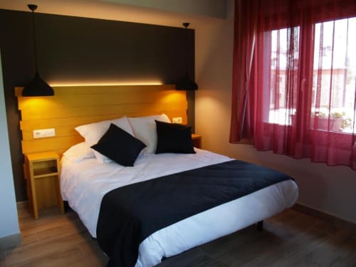 Habitación moderna del Hotel Llibrada con cabecera amarilla, lámparas colgantes negras y vistas a la montaña desde ventanas con cortinas rojas