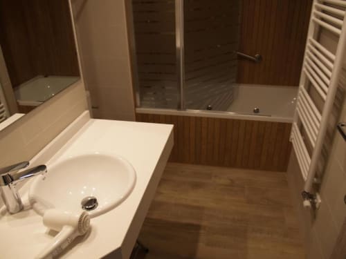 Baño moderno en apartamento de Benasque con lavabo blanco, cabina de ducha y paredes con acabado en madera