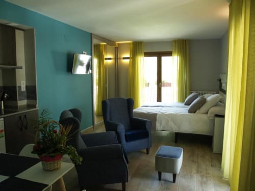 Moderno apartamento estudio en Benasque con paredes turquesas, sillones azules, cama con vistas a la montaña y cortinas amarillas
