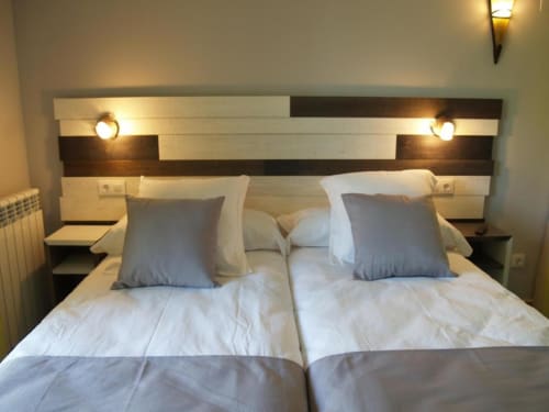 Moderno dormitorio doble con dos camas individuales, cabecero a rayas, almohadas azules y apliques de pared en Hotel Llibrada, Benasque