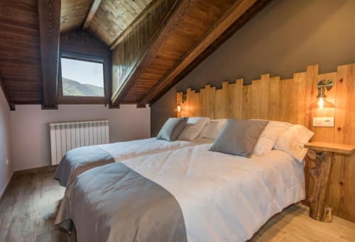 Acogedor dormitorio de montaña en Hotel Llibrada en Benasque con vigas de madera, dos camas y vistas alpinas a través de claraboya