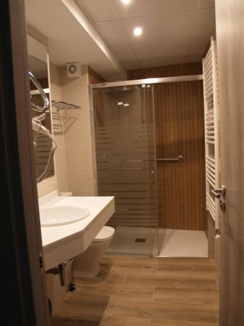 Baño moderno en El Puente Apartments, Benasque con ducha amplia, lavabo blanco, inodoro y pisos con efecto madera