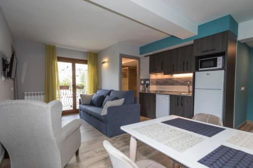 Moderna zona de estar con cocina americana, sofá azul, mesa de comedor y acceso a terraza en Hotel Llibrada, Benasque