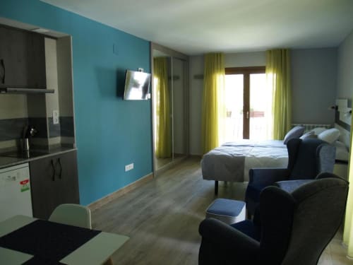 Apartamento estudio en Benasque con paredes turquesas, cama, sala de estar, cocina y balcón con vistas a la montaña