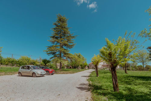 Parking en gravier de Vila Cabanes 46 avec deux voitures, arbres verdoyants et bâtiments en pierre en Montat