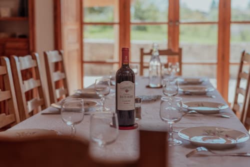 Salle à manger élégante à Vila Cabanes 46 avec bouteille de vin, couverts et vue sur la campagne par les grandes fenêtres