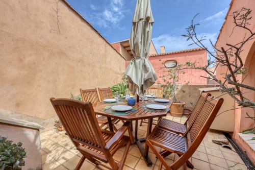 Terrasse de la Société des Palmiers à Porquerolles avec table en bois, chaises et parasol surplombant la Méditerranée