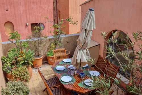 Terrasse spacieuse à la Société des Palmiers à Porquerolles avec table de salle à manger, chaises en bois, plantes en pots et store rétracté