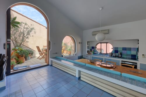 Cuisine moderne aux comptoirs bleus, plan de travail en bois et baie cintrée ouvrant sur la terrasse de Porquerolles et la mer
