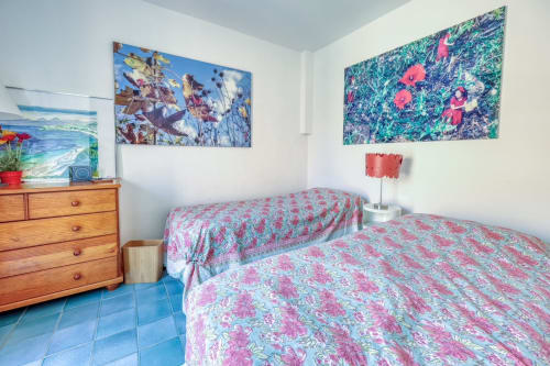 Chambre lumineuse avec lits jumeaux, literie aux motifs floraux roses, commode en bois et tableaux colorés à la Société des Palmiers