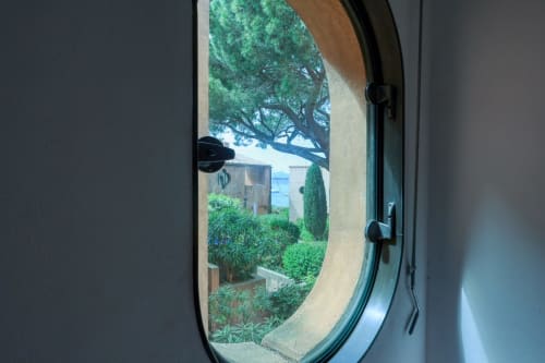 Vue depuis un hublot de l'appartement Société des Palmiers à Porquerolles, surplombant les jardins luxuriants et la Méditerranée