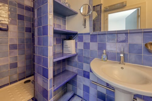 Salle de bains carrelée de bleu avec lavabo, miroir et rangements à l'appartement Société des Palmiers à Porquerolles
