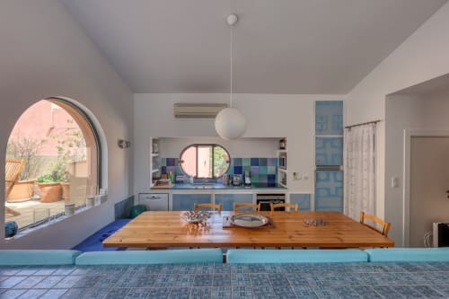 Cuisine et salle à manger modernes avec accents bleus, table en bois et baie vitrée cintrée donnant sur le jardin de Porquerolles