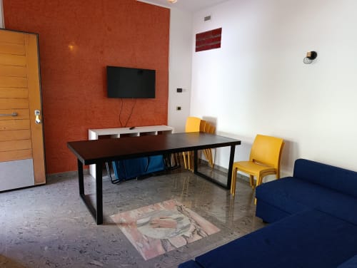 Casa Bertila apartment dining area with black table, yellow chairs, TV, and navy sofa in Ancona