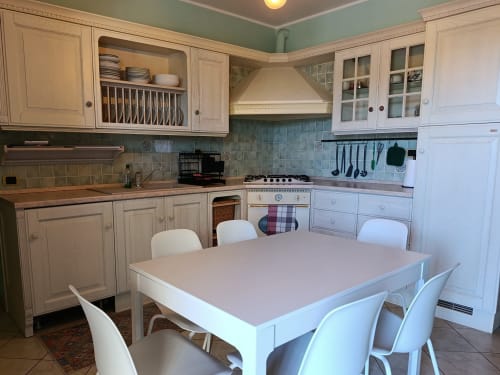 Bright kitchen-dining area in Casa Bertila apartment, Ancona with white cabinetry, teal backtile, and dining table