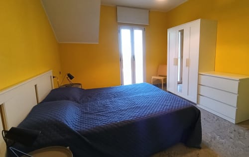 Bright yellow bedroom at Casa Bertila, Ancona apartment with blue bed and white furniture